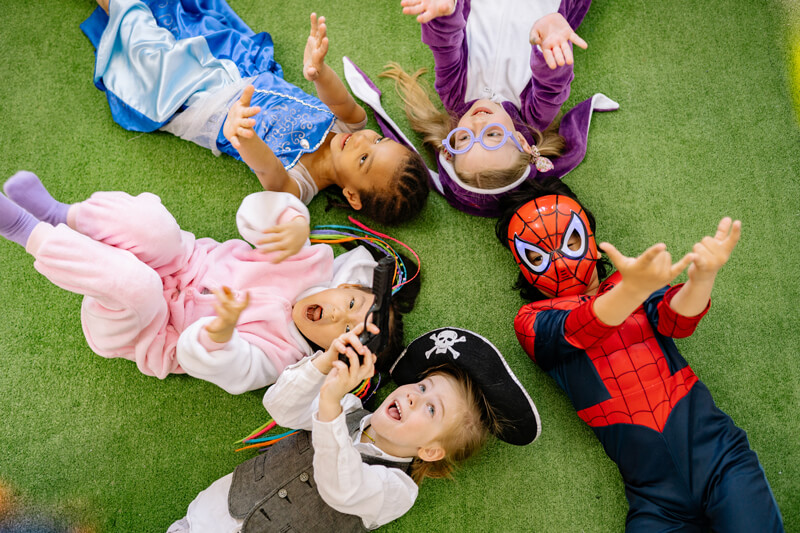 Children lying on grass in costumes and smiling
